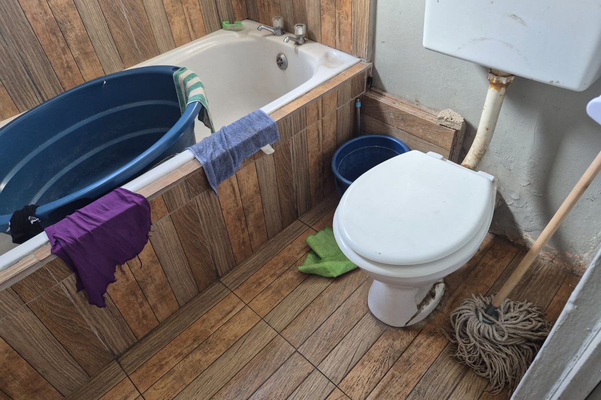 A dated bathroom featuring a bathtub and toilet with wood-look tile finishes, requiring significant maintenance and renovation to improve its condition.