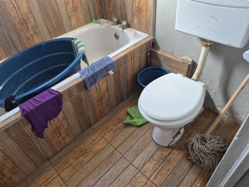 A dated bathroom featuring a bathtub and toilet with wood-look tile finishes, requiring significant maintenance and renovation to improve its condition.