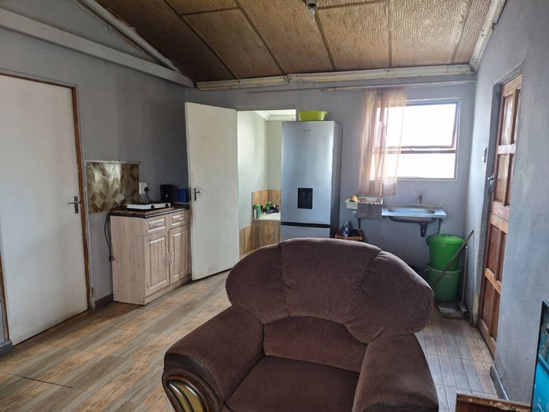 Open plan living area featuring tiled flooring, exposed beam ceiling, and a compact kitchenette area with a stainless steel sink and cabinetry.
