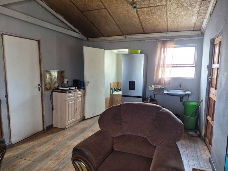 Open plan living area featuring tiled flooring, basic kitchen cabinetry with a sink, and exposed ceiling panels, offering potential for modernization.