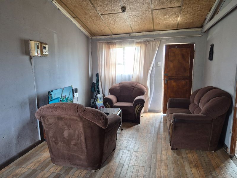 A living room featuring tiled flooring and timber ceiling panels, requiring cosmetic updates and maintenance to the ceiling and electrical fixtures.