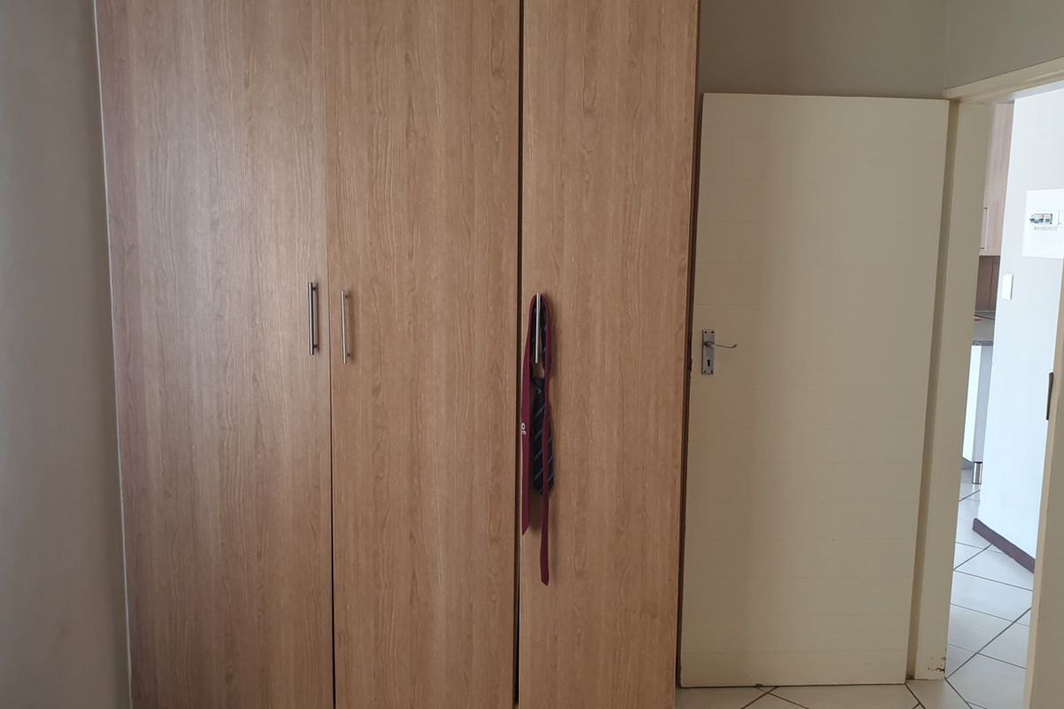 A bedroom featuring light wood-finish built-in cupboards and tiled flooring, with a doorway leading to an adjacent living area.