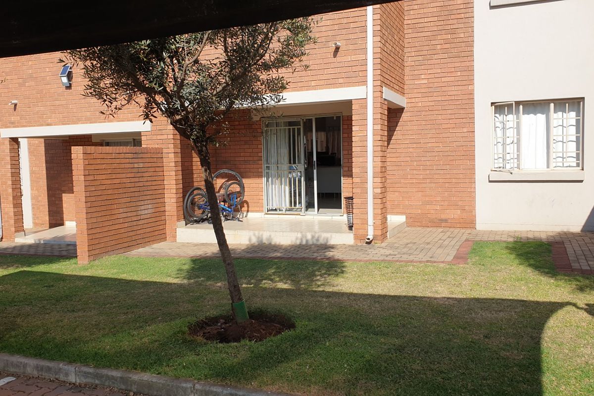 Rear view of the apartment featuring a brick facade, a paved patio area, and a small private lawn.