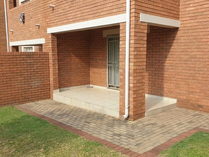 A covered brick patio area with tiled flooring and adjacent paved walkway, providing direct access to the apartment interior.