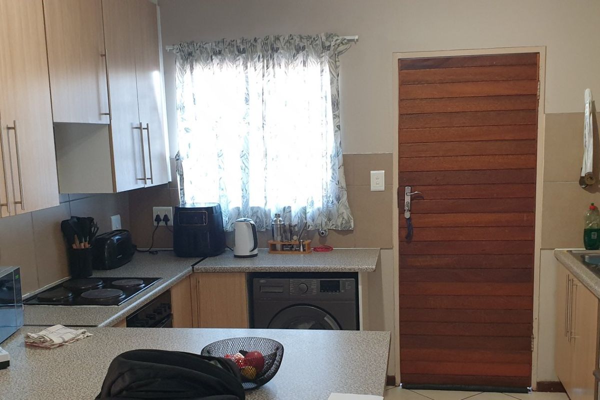 Functional kitchen featuring laminate cabinetry, stone-look countertops, electric hob, built-in oven, and integrated washing machine with a timber exterior door.
