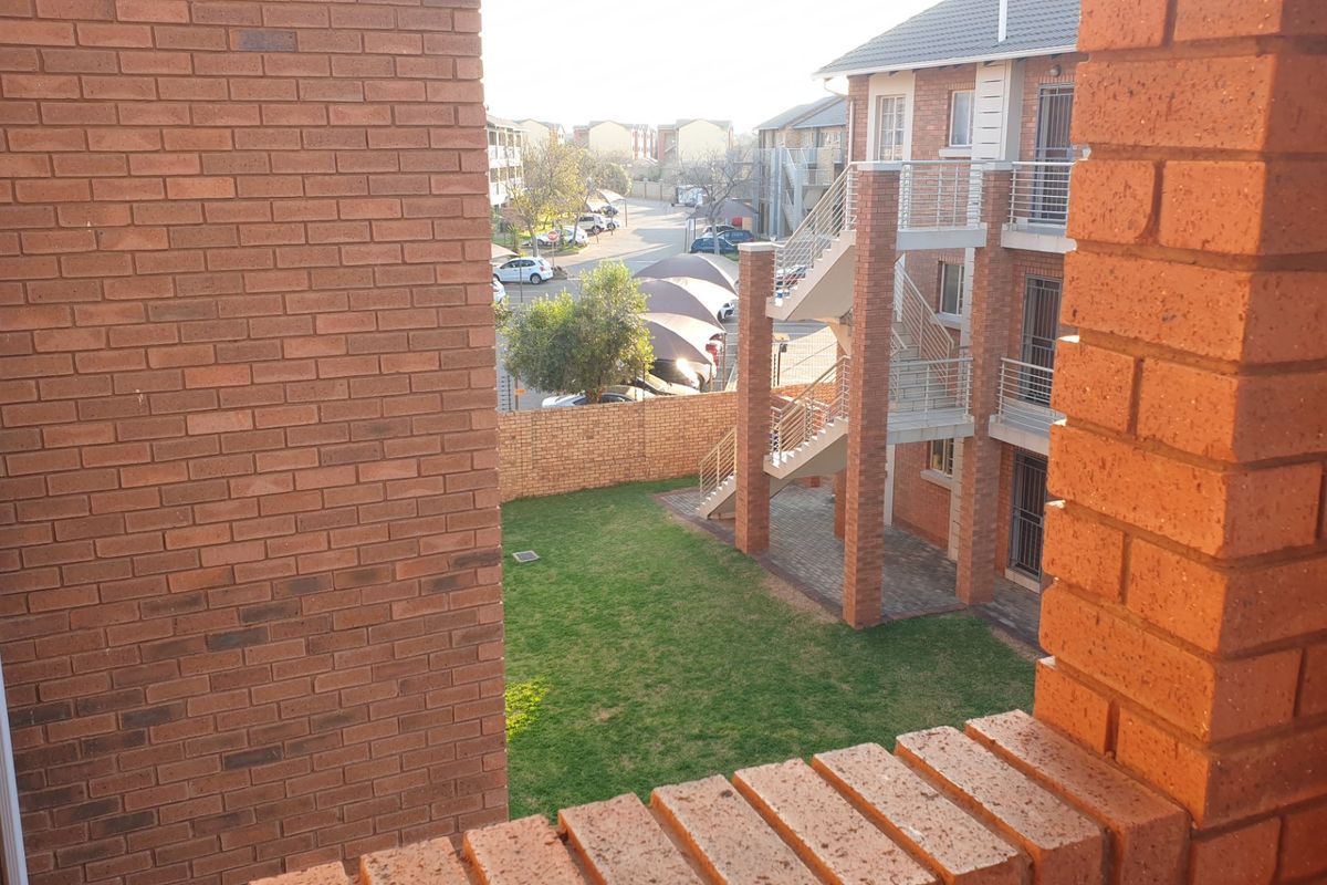 View of the apartment complex rear exterior, featuring brick facade, communal lawn area, and external staircase access.