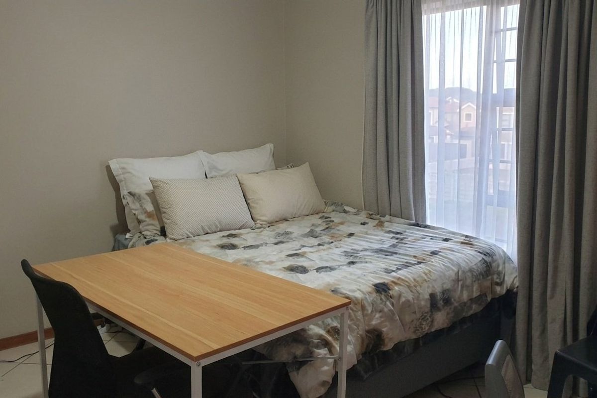 A functional bedroom featuring tiled flooring and a window with installed curtain tracks, providing natural light and a neutral backdrop.