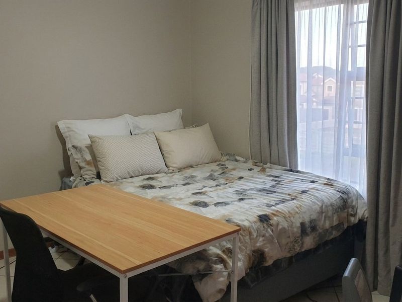 A functional bedroom featuring tiled flooring and a window with installed curtain tracks, providing natural light and a neutral backdrop.
