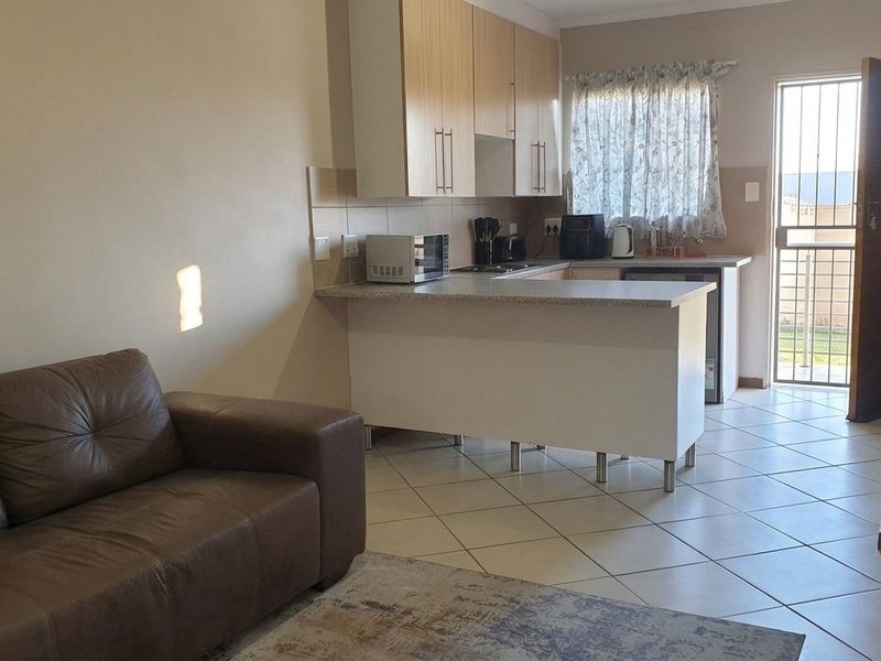 Open-plan living area featuring a functional kitchen with laminate cabinetry, tiled flooring, and direct access to an exterior door with a security gate.