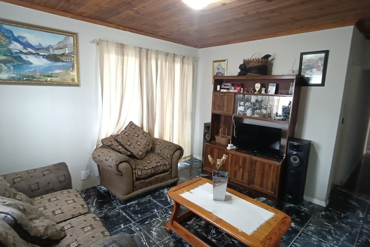 A living room featuring a timber-paneled ceiling and dark marble-effect floor tiles, providing a dated but functional living space.