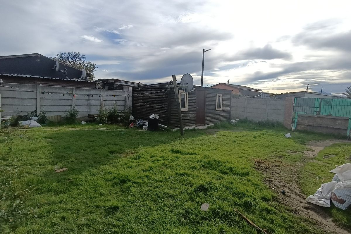Rear garden area featuring a lawn, precast concrete boundary walls, and a timber outbuilding structure.