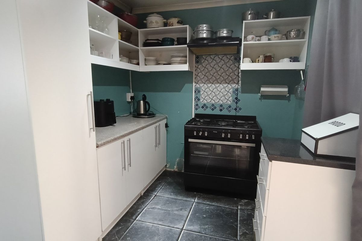 A compact kitchen featuring white cabinetry, dark stone countertops, a black gas stove with extractor fan, and decorative tiled splashback.
