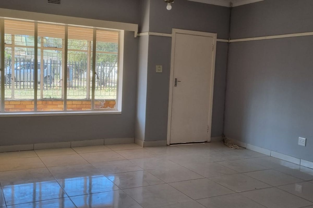 A spacious, empty living room featuring neutral grey walls, tiled flooring, and a large window providing natural light.