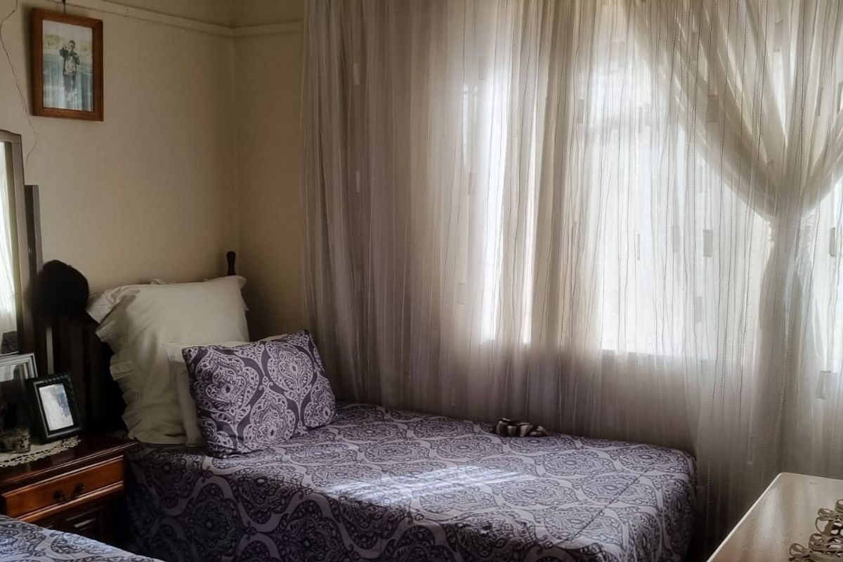 A bedroom featuring natural light through window curtains and visible wall cracking requiring maintenance.