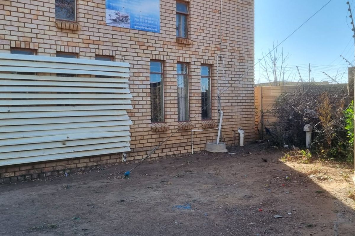 Rear exterior view of a face brick commercial building featuring perimeter electric fencing and a damaged privacy screen over the windows.