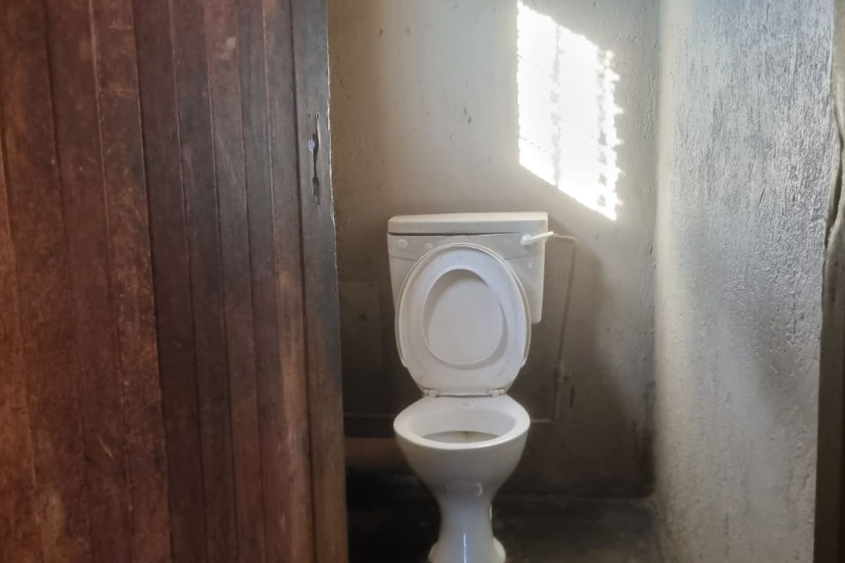 A small, basic bathroom featuring a standard toilet and a wooden door, requiring cosmetic updates and wall refinishing.