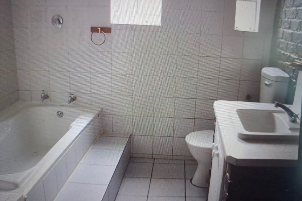 A dated bathroom featuring a built-in bathtub, vanity basin, and toilet with original ceramic tiling throughout.