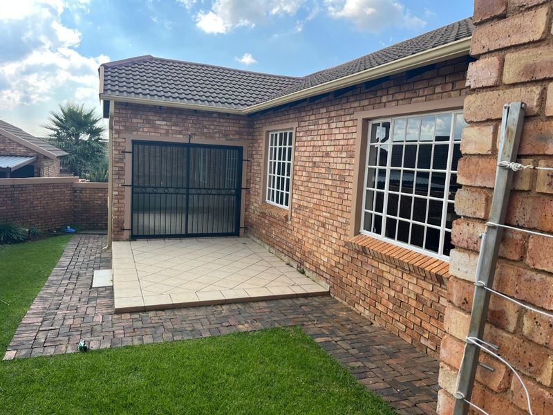 A rear exterior view of a townhouse featuring a face brick facade, a small tiled patio area, and paved garden pathways.