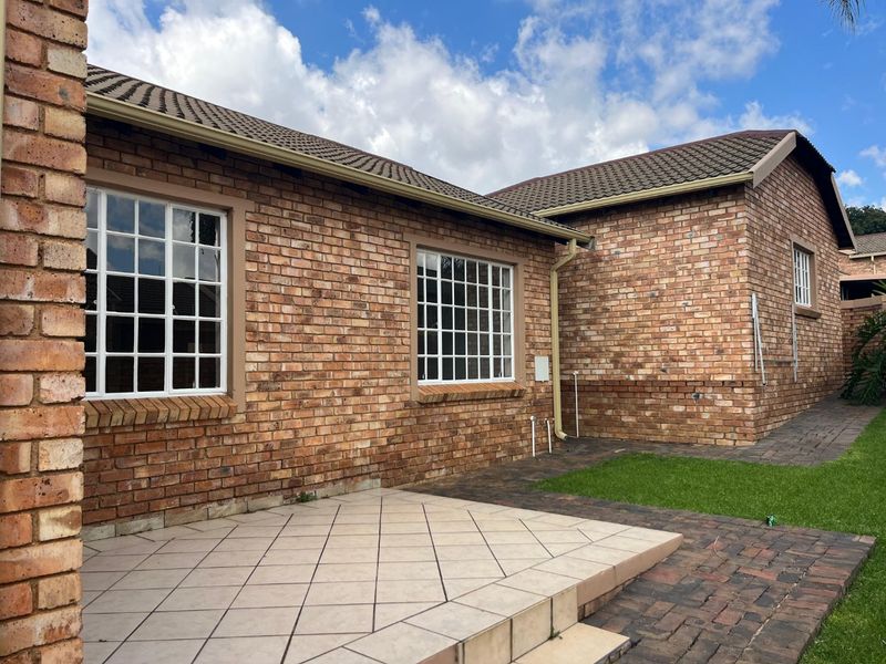 Rear view of the townhouse featuring a face brick facade, tiled roof, paved patio area, and a small lawn.