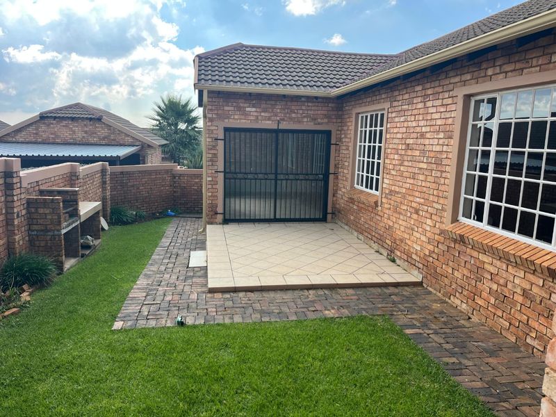 Rear exterior view of the townhouse featuring a paved patio, built-in braai area, and a private garden with brick boundary walls.
