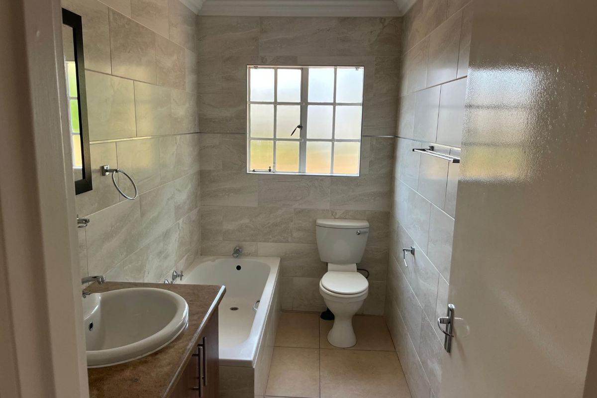 A clean, neutral-toned bathroom featuring a built-in vanity, bathtub, and toilet with modern wall and floor tiling.