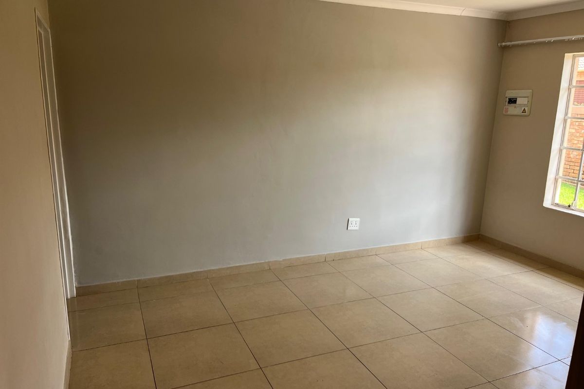 An empty bedroom featuring neutral wall paint, tiled flooring, and a window with security bars, providing a clean and versatile space.