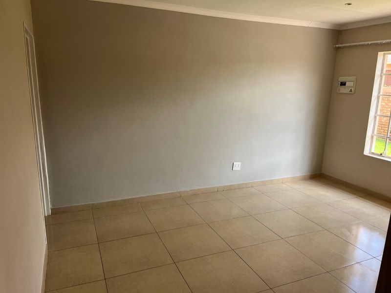 An empty bedroom featuring neutral wall paint, tiled flooring, and a window with security bars, providing a clean and versatile space.
