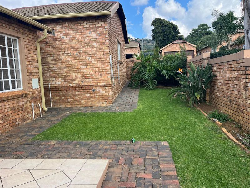A private rear garden featuring a well-maintained lawn, paved walkway, and tiled patio area, enclosed by face brick boundary walls.