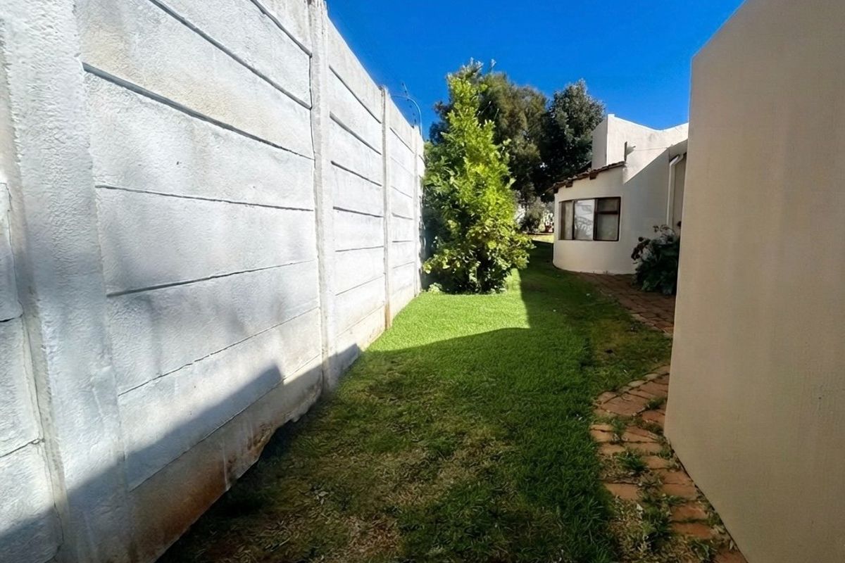 A side garden area featuring a precast concrete boundary wall with electric fencing, a paved walkway, and a grass lawn.