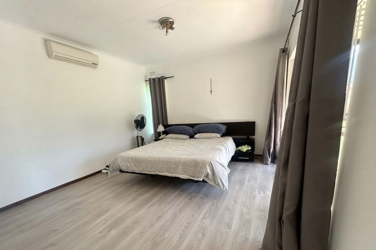 A spacious bedroom featuring light-toned laminate flooring, a wall-mounted air conditioning unit, and neutral walls, providing a clean and functional living space.