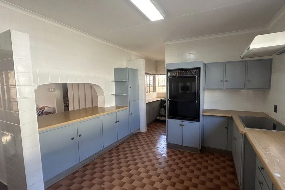 A spacious, dated kitchen featuring built-in cabinetry, laminate countertops, a built-in oven, and an electric hob, offering significant potential for modern renovation.