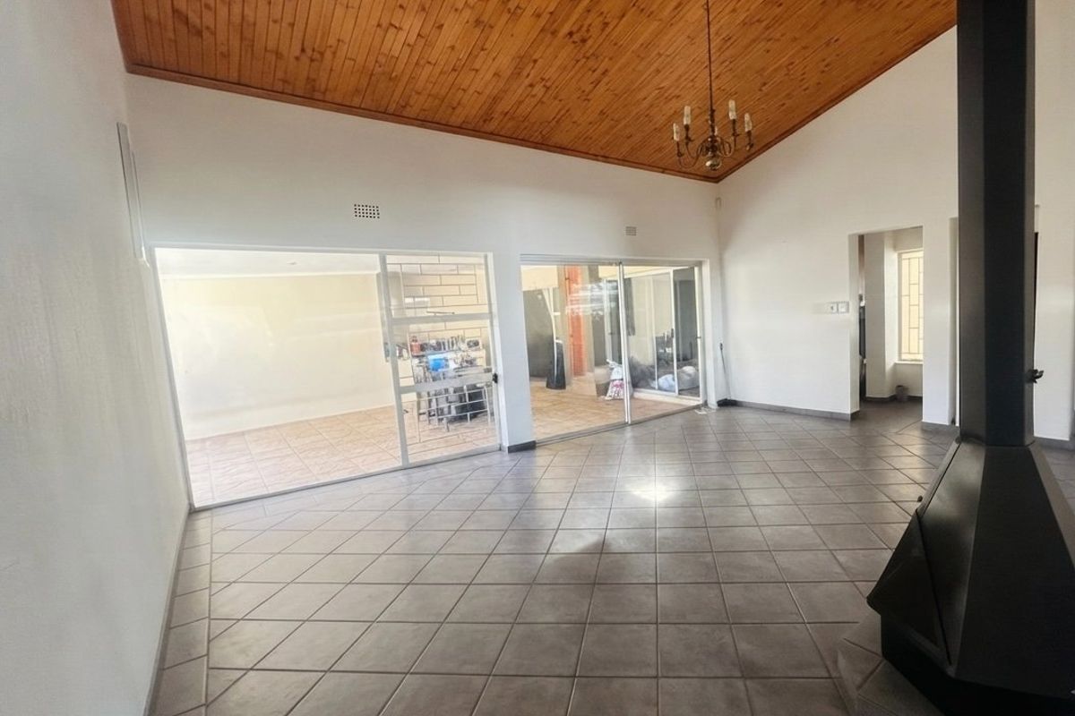 Spacious living area featuring a vaulted timber ceiling, tiled flooring, and a prominent freestanding fireplace, with large sliding doors opening to the patio.
