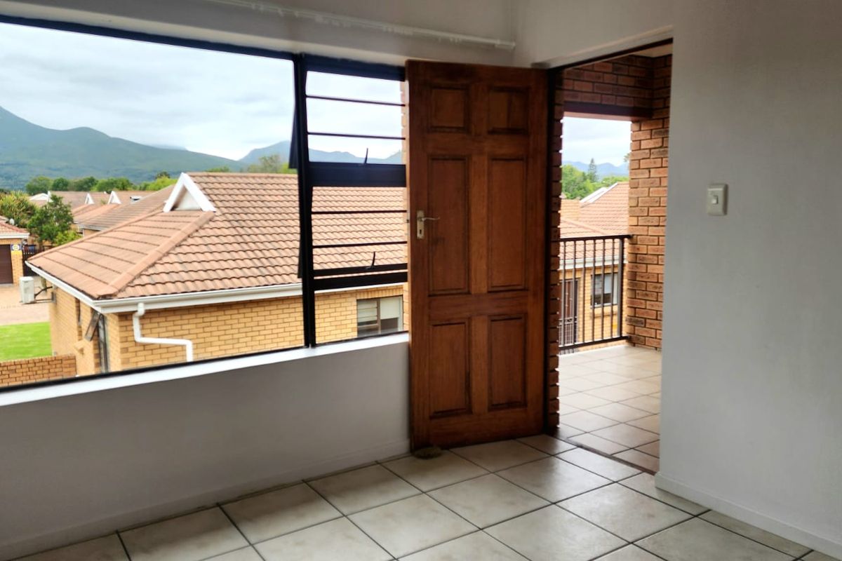 An empty living area featuring tiled flooring, large windows with mountain views, and direct access to a private balcony.