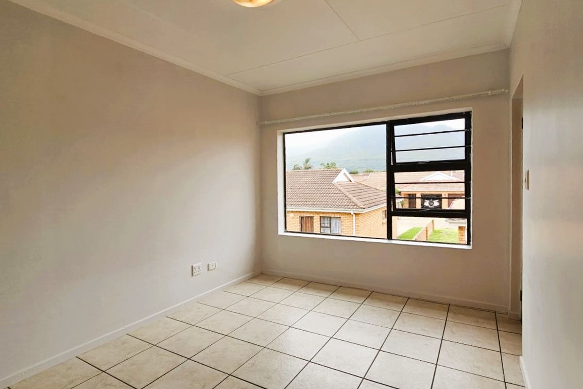 A bright, empty bedroom featuring neutral wall finishes, tiled flooring, and a large window with views of the surrounding neighbourhood.