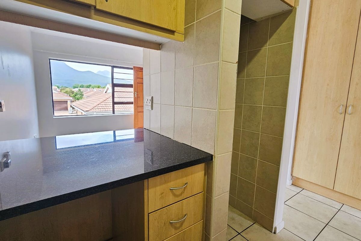 A functional kitchen area featuring granite countertops, tiled splashbacks, and built-in cabinetry, with an open view towards the living space and exterior.