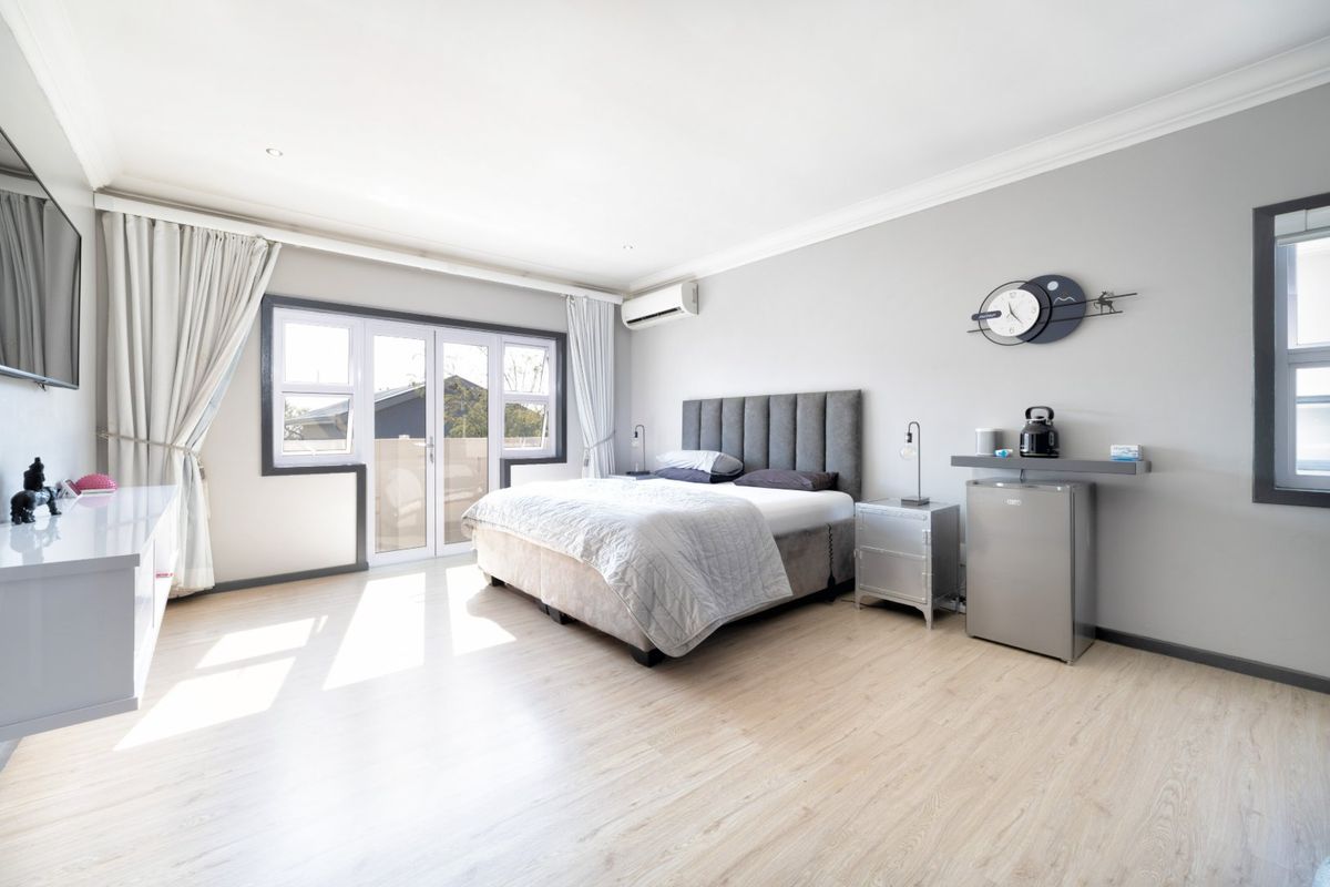 Spacious bedroom featuring light laminate flooring, neutral walls, coving, and direct access to an outdoor area through glass french doors.