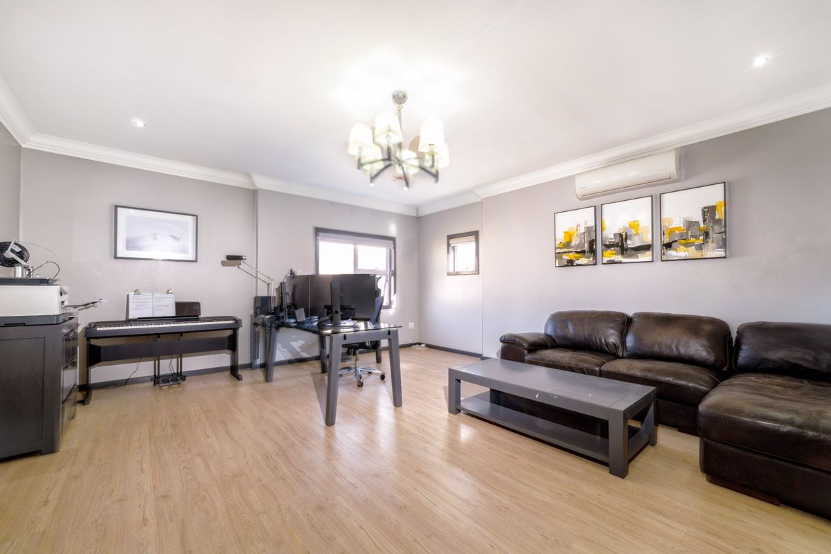 A well-maintained living area featuring light laminate flooring, cove cornicing, recessed lighting, and a wall-mounted split-system air conditioner.