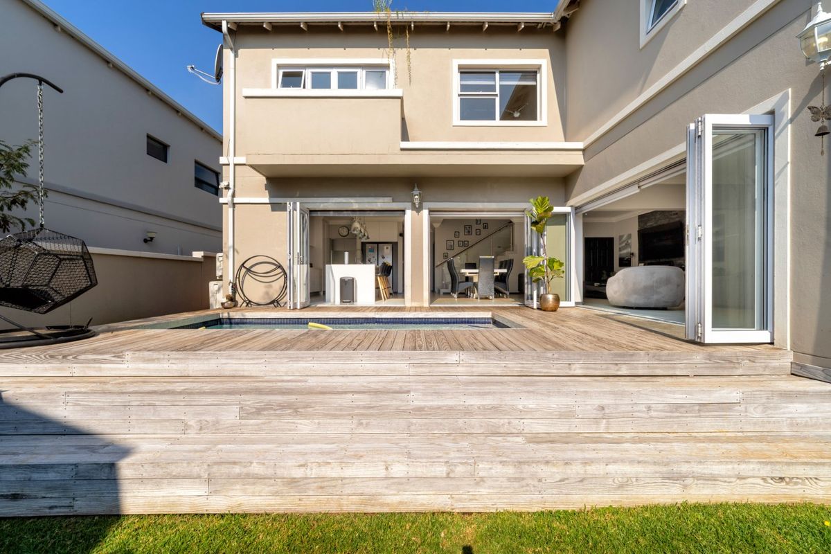 Rear exterior view featuring a timber deck, integrated swimming pool, and large bi-fold doors providing seamless indoor-outdoor flow to the living and kitchen areas.