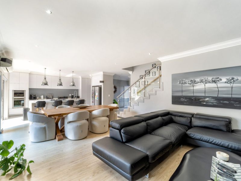 Spacious open-plan living and dining area featuring a modern kitchen with integrated appliances, light wood flooring, and a contemporary staircase with glass balustrades.