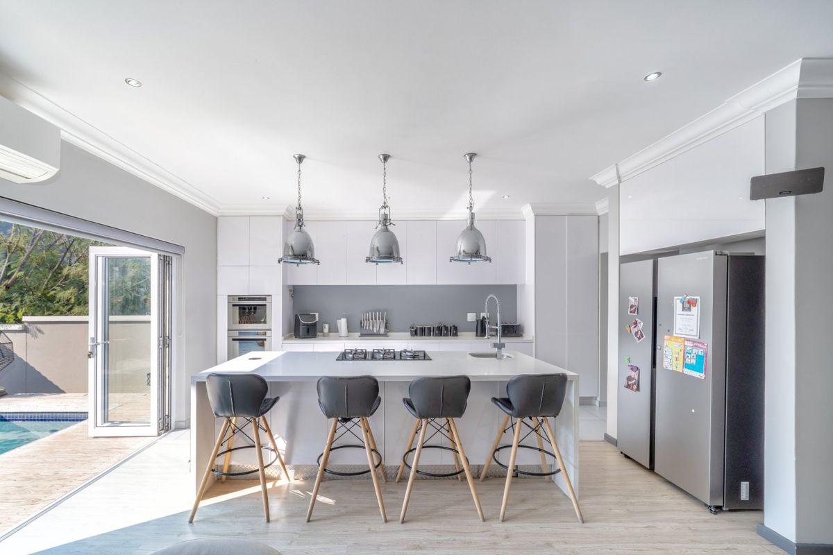 Modern kitchen featuring a large central island with gas cooktop, integrated appliances, sleek cabinetry, and direct access to the outdoor pool area via bi-fold doors.