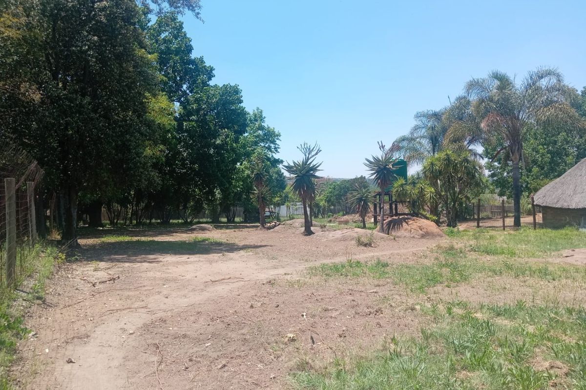 A spacious, undeveloped residential plot featuring mature trees, natural landscaping, and an existing water tank installation.