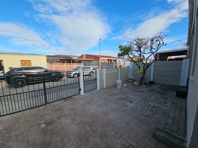 A paved front courtyard area featuring a secure wrought iron gate and precast concrete boundary walling.