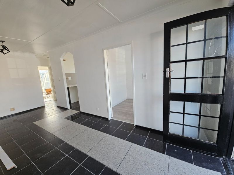 A bright, empty hallway featuring contrasting black and grey tiled flooring, an arched entryway, and a black-framed glass panelled door.