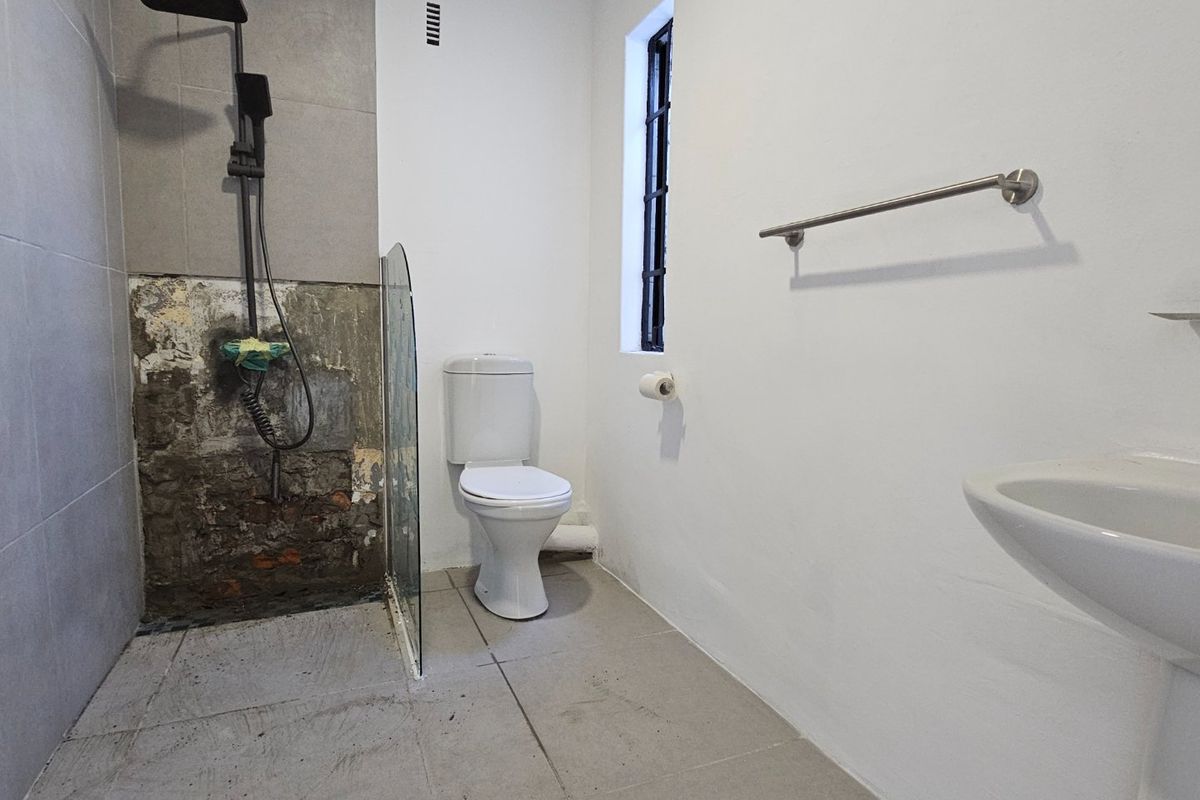 A bathroom featuring a pedestal basin, toilet, and shower area with exposed brickwork requiring tiling and renovation.