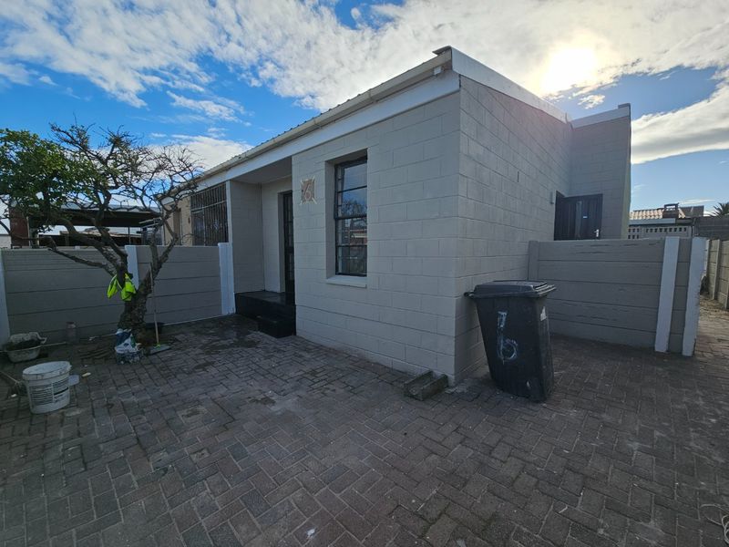 Front exterior view of a single-story house featuring concrete block construction, a paved driveway, and perimeter walling.