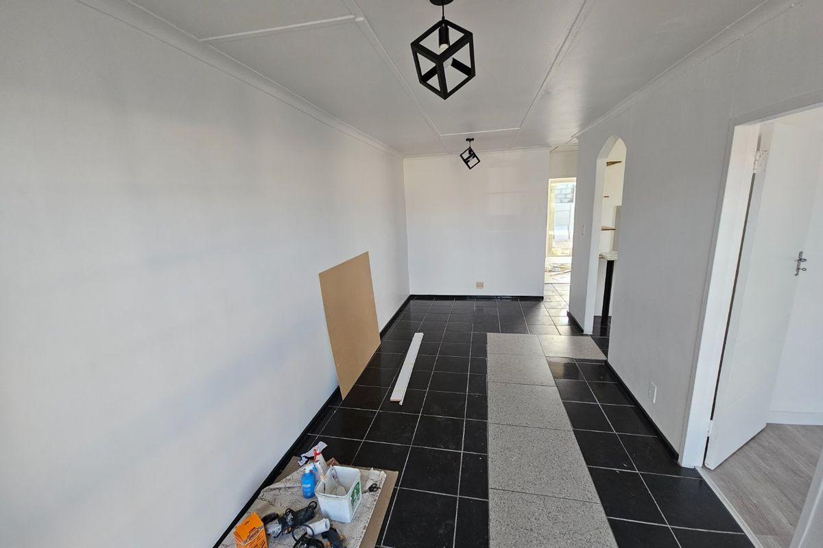An empty living area featuring black tiled flooring, modern geometric pendant lighting, and an arched entryway, currently undergoing minor renovations.