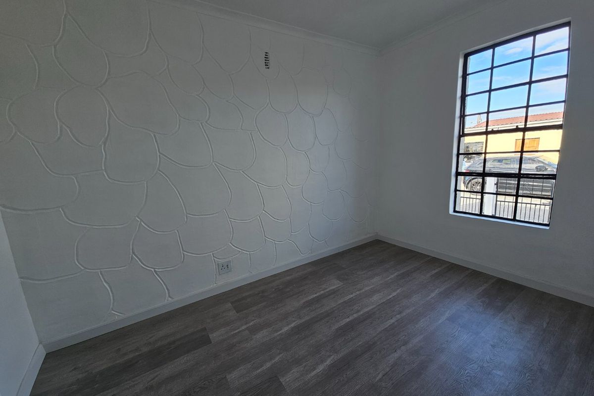 A bright, empty bedroom featuring modern grey laminate flooring and a unique textured feature wall with a grid-pattern window.