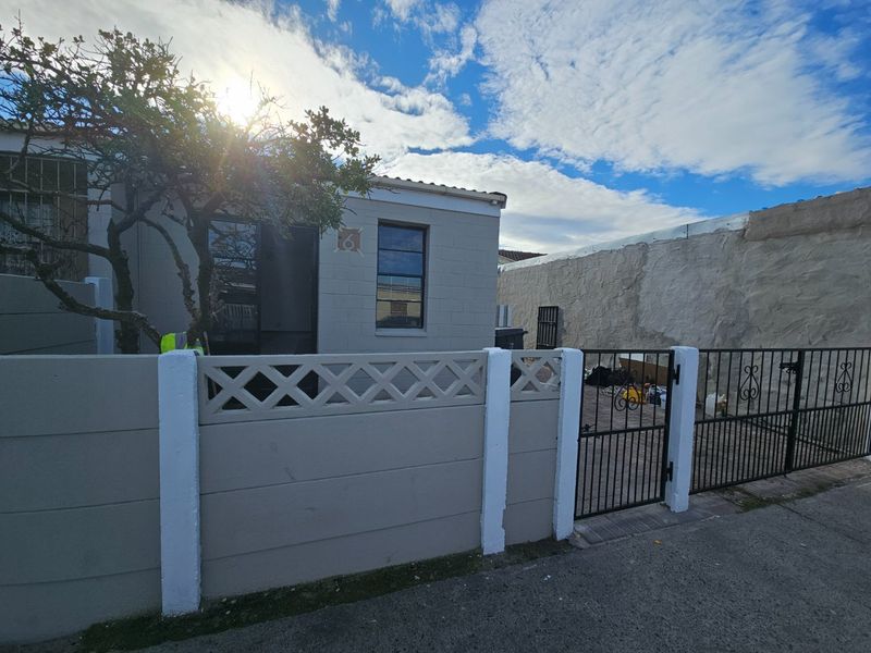 Front exterior view of the property featuring a paved driveway, wrought iron gate, and a precast concrete boundary wall.