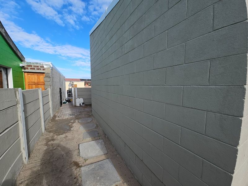 A side passage featuring a painted concrete block wall, precast boundary fencing, and stone pavers leading toward the rear of the property.