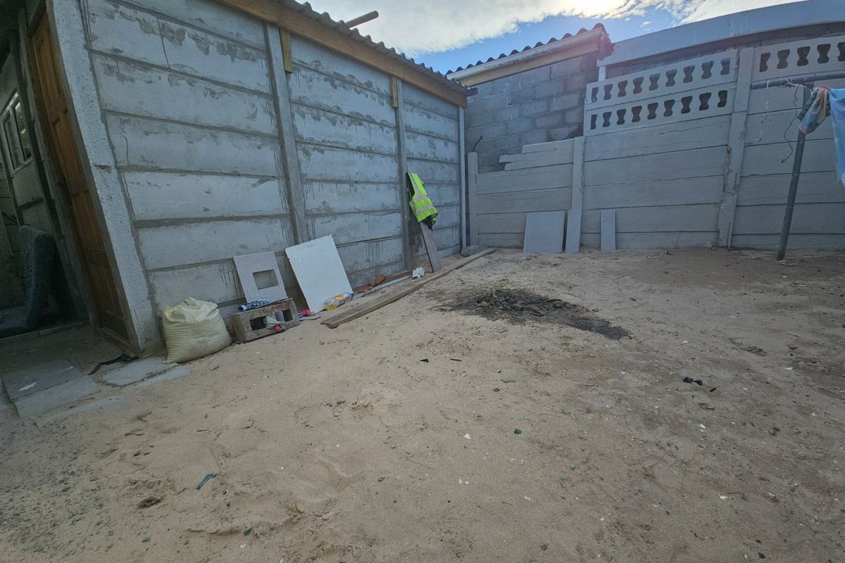 A rear outdoor area featuring precast concrete boundary walls and sandy ground, currently in an unfinished state requiring landscaping and maintenance.